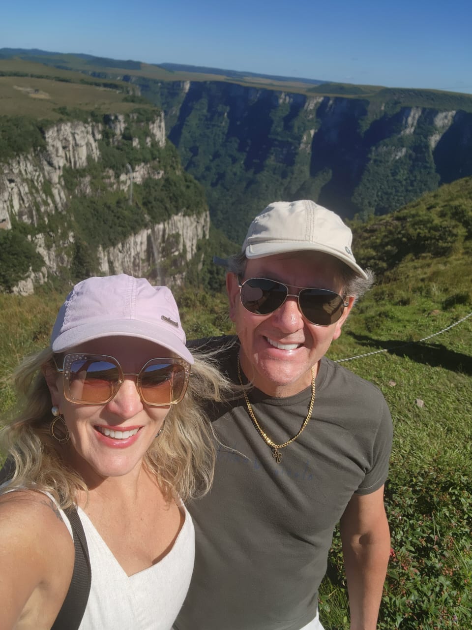 Teresa e o marido, autores do Quero Me Mexer, de boné e óculos de sol em uma trilha, com um cânion ao fundo